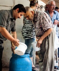 A man pouring water from a jug into a bucket for another man, who is placed in front of a line of people.