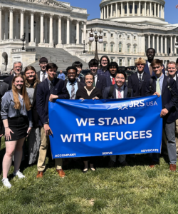 A group of people standing in front of the US Capitol building with a sign that says, 'we stand with refugees/'